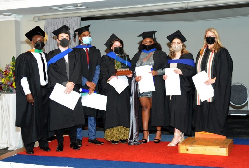 A group of AAA School of Advertising students in their graduation outfits and caps holding their degree certificates